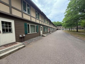 A row of motel rooms with a gravel driveway and trees in the background.