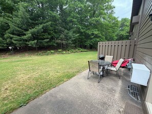 A backyard with a patio table and chairs, a wooden fence, and a grassy lawn.