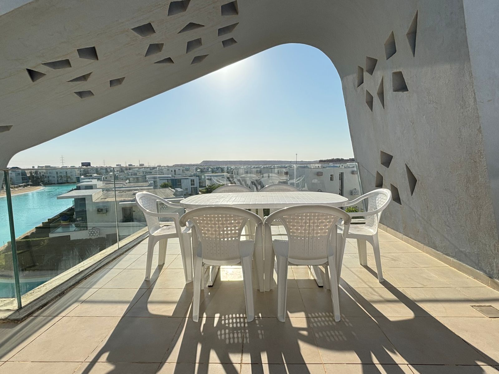 A terrace with a table and chairs, overlooking a swimming pool and buildings.