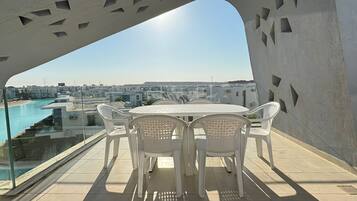 A terrace with a table and chairs, overlooking a swimming pool and buildings.