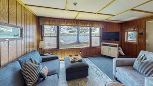 A cozy living room with a sofa, ottoman, and a television. - Cozy, lakefront cottage w/ a firepit,kayak,shared patio, gas grill, & free WiFi (Eagle River)