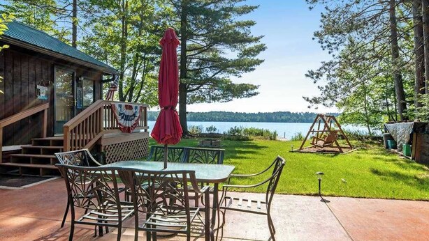 A wooden cabin with a patio, a swing set, and a view of a lake. - Cozy, lakefront cottage w/ a firepit,kayak,shared patio, gas grill, & free WiFi (Eagle River)