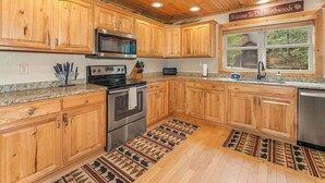 A kitchen with wooden cabinets, a microwave, stove, and a sink. - Lakefront home with private dock, firepit, playground & lake views (Eagle River)