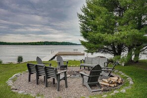 A lakeside seating area with Adirondack chairs, a fire pit, and a dock extending into the water.