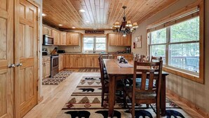 A wooden interior with a dining table, chairs, a chandelier, and a view of the outdoors. - Lakefront home with private dock, firepit, playground & lake views (Eagle River)