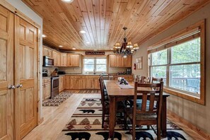 A wooden interior with a dining table, chairs, a chandelier, and a view of the outdoors.