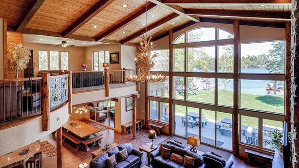 A spacious interior with a high ceiling, large windows, and a wooden staircase. - Luxury lakefront home with high-speed WiFi, dock, private beach, & theater room (Eagle River)