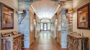 A hallway with stone walls, wooden flooring, and framed artwork on the walls. - Luxury lakefront home with high-speed WiFi, dock, private beach, & theater room (Eagle River)