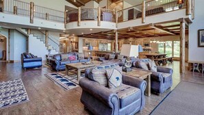 A spacious living area with a high ceiling, wooden beams, a staircase, and a large chandelier. - Luxury lakefront home with high-speed WiFi, dock, private beach, & theater room (Eagle River)