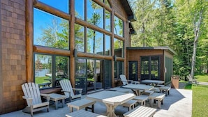 A building with large windows, outdoor seating, and a patio area. - Luxury lakefront home with high-speed WiFi, dock, private beach, & theater room (Eagle River)