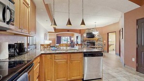Une cuisine avec des meubles en bois, un lave-vaisselle, une cuisinière et des luminaires suspendus.