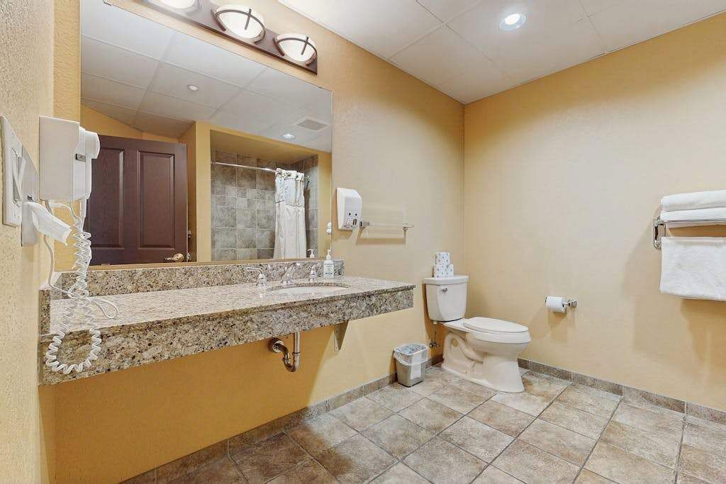 A bathroom with a granite countertop sink, a toilet, a mirror, and a towel rack.