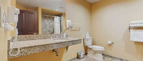 A bathroom with a granite countertop sink, a toilet, a mirror, and a towel rack.