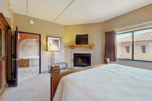 A hotel room with a bed, a fireplace, a TV, and a view of the outside.