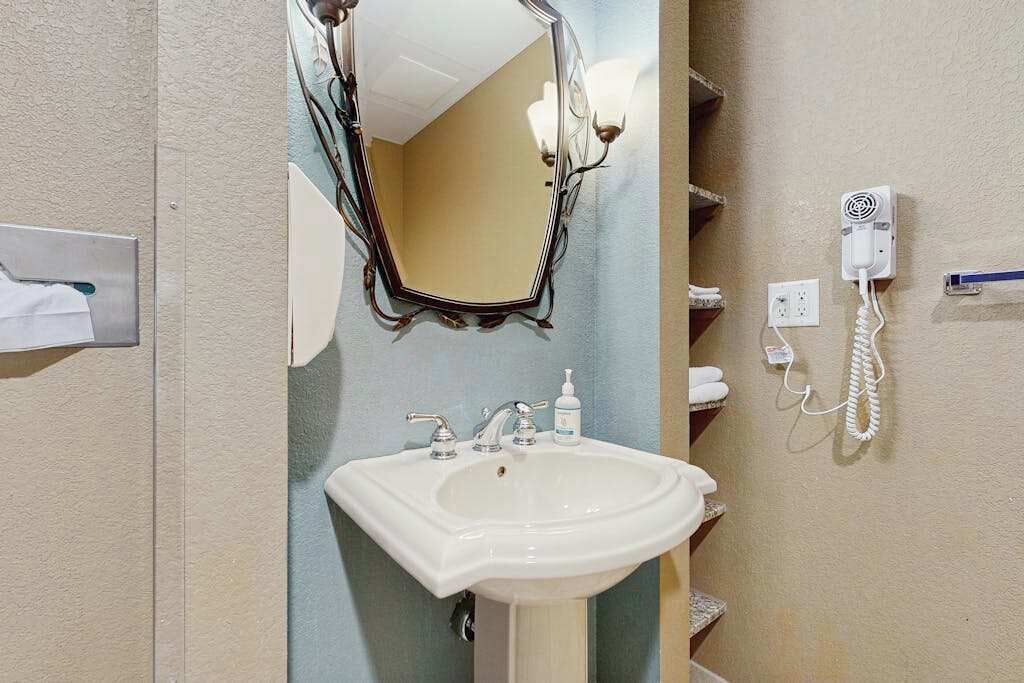 A bathroom with a white sink, a mirror, a towel rack, a hairdryer, and a phone.