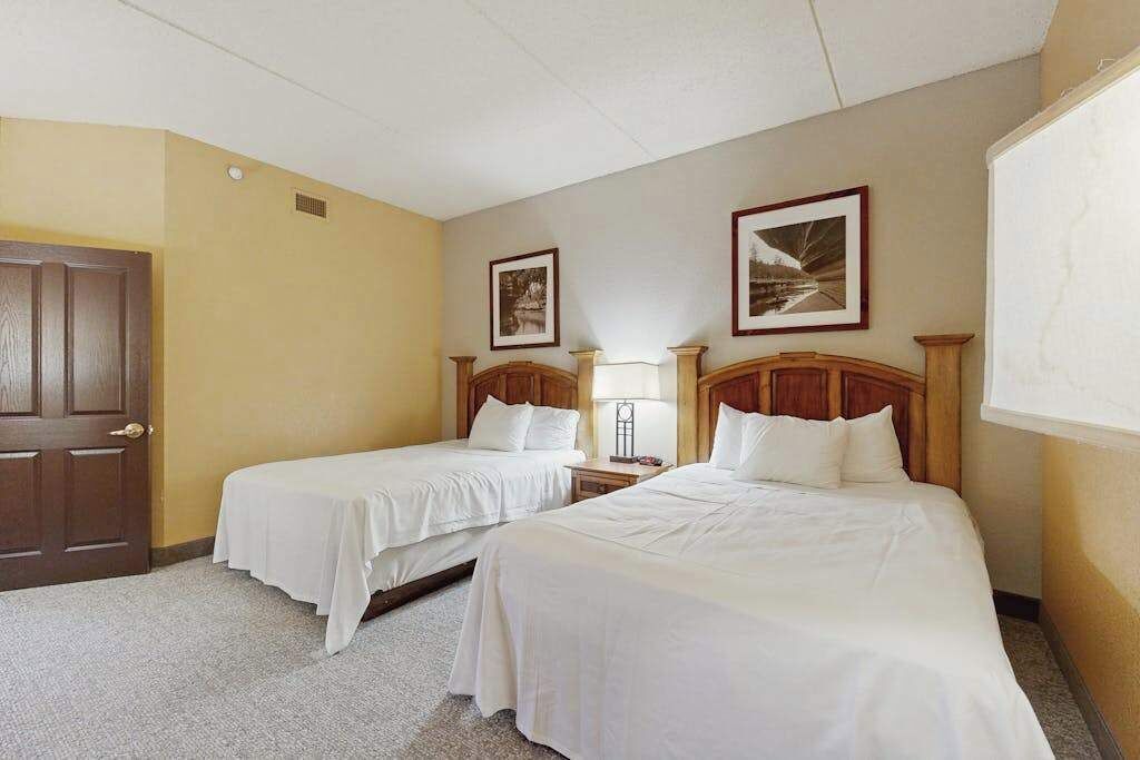 A hotel room with two single beds, a wooden door, and two framed pictures on the wall.