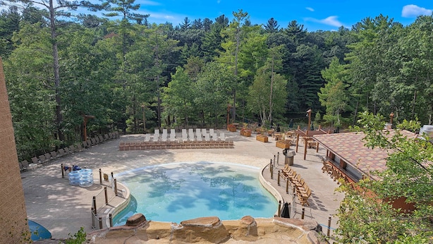 Un espace piscine doté de chaises longues, d’un jacuzzi et bordé d’une forêt naturelle.