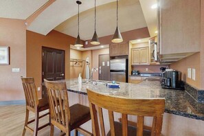 A kitchen with a central island, wooden chairs, pendant lights, and a refrigerator.