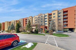 Un hotel de varios pisos con estacionamiento, un coche rojo y suelo cubierto de nieve.