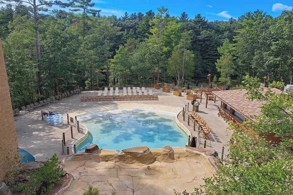 Una piscina rodeada por una terraza de madera, con un bosque de fondo.