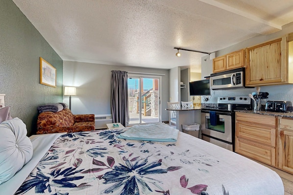 Quarto de hotel com cama, sofá, mesa de jantar e cozinha equipada com micro-ondas, forno e armários.