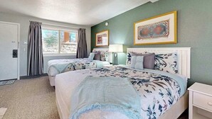 A hotel room with two beds, a window with curtains, a bedside table, and framed pictures on the wall.