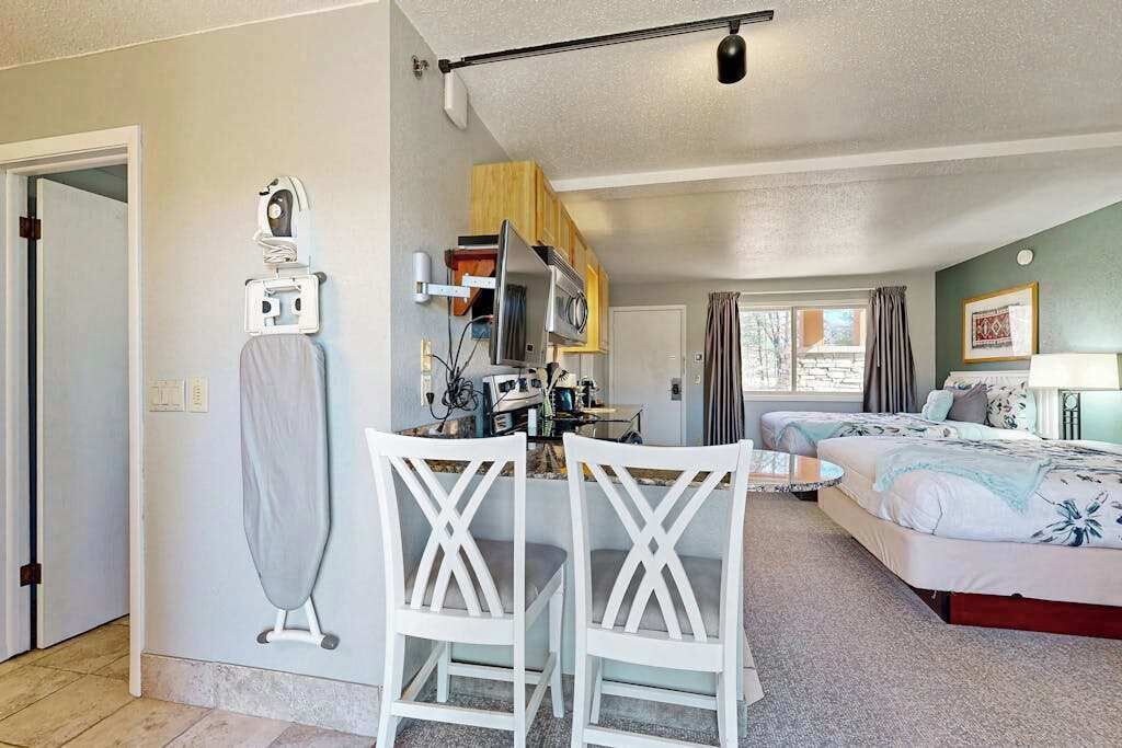 A compact room with a kitchenette, a dining area with two chairs, a bed, and a window with curtains.