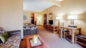 Een hotelkamer met een bank, een bed met quilt, een eettafel met stoelen, een televisie en een lamp.