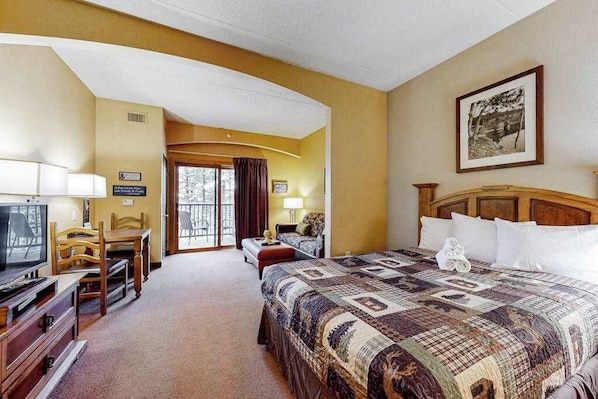 Une chambre d’hôtel avec un grand lit, une télévision, un bureau avec une chaise et un balcon.