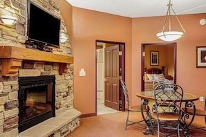A room with a stone fireplace, a television mounted on the wall, a dining table with chairs, and a door leading to another room. - Family Getaway at Chula Vista Discount Perks (Wisconsin Dells)
