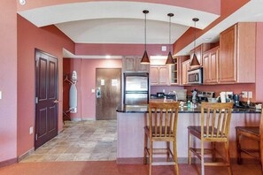 A kitchen with wooden cabinets, a refrigerator, a microwave, and a bar area with two wooden chairs. - Resort Condo with Discount Adventure Perks in the Dells (Wisconsin Dells)