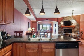 A kitchen with wooden cabinets, a granite countertop, a dishwasher, pendant lighting, a stone fireplace, and a dining area with chairs and a table. - Resort Condo with Discount Adventure Perks in the Dells (Wisconsin Dells)