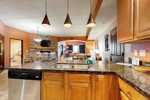 A kitchen with granite countertops, wooden cabinets, a dishwasher, and pendant lighting.