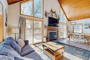 A spacious living room with a fireplace, a television, and a dining area with white chairs. - Lakefront condo with beach access, firepit, games, fireplace, & dock (Wisconsin Dells)
