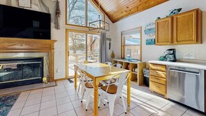 Tunnelmallinen keittiö, jossa on puinen pöytä, tuolit, takka ja suuri ikkuna.