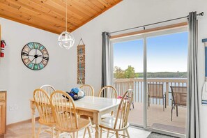A dining area with a wooden table and chairs, a decorative clock, and a view of the outdoors through a sliding glass door.