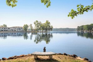 A calm lake with a bench, trees, and a building in the background.