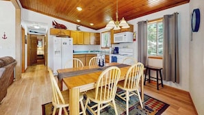 A wooden ceiling, a dining table with chairs, a kitchen with appliances, and a window with curtains. - Lakefront retreat with panoramic views, large backyard, & direct beach access (Wisconsin Dells)