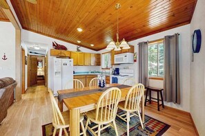 Un plafond en bois, une table à manger avec des chaises, une cuisine équipée et une fenêtre avec des rideaux.