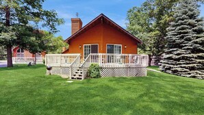 A wooden cabin with a deck, surrounded by a well-maintained lawn and trees. - Lakefront retreat with panoramic views, large backyard, & direct beach access (Wisconsin Dells)