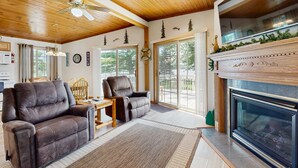 A living room with a fireplace, wooden ceiling, and a large window. - Lakefront retreat with panoramic views, large backyard, & direct beach access (Wisconsin Dells)