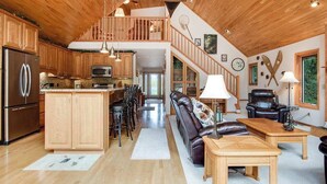 A spacious kitchen with wooden cabinets, a stainless steel refrigerator, and a dining area with a leather sofa and wooden tables. - Dog-friendly lakefront getaway with dock, firepit, wet bar, game room, & AC (Eagle River)