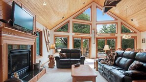 A spacious living room with a fireplace, leather sofas, and large windows. - Dog-friendly lakefront getaway with dock, firepit, wet bar, game room, & AC (Eagle River)