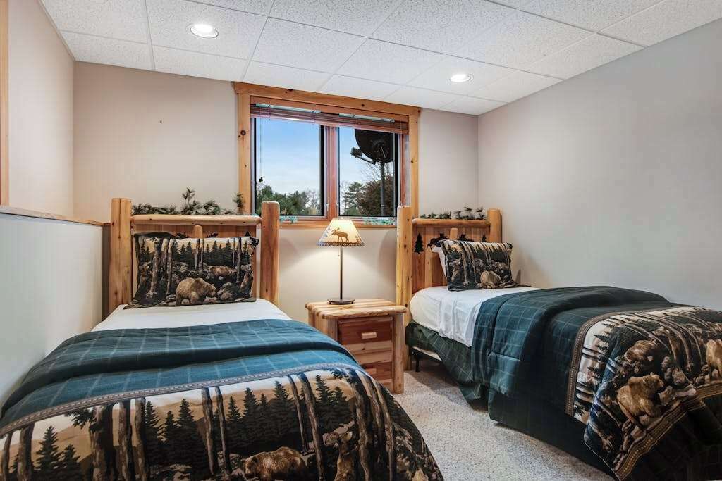 Une chambre avec deux lits, une fenêtre, une lampe et une petite table.