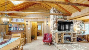 Ein Holzinterieur mit Kamin aus Stein, einem Fernseher und einem Essbereich.
