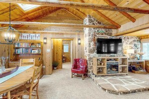 A wooden interior with a stone fireplace, a television, and a dining area. - Charming lakefront home with dock, fireplace, streaming, lake views, W/D, & AC (Conover)