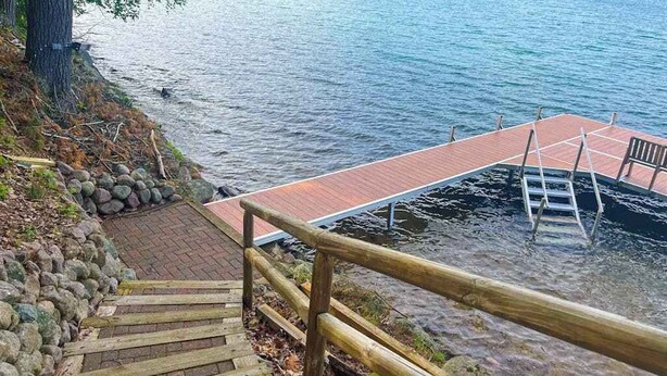 Eine Holzstele reicht in einen See, mit einer Steinmauer und einer Holztreppe, die zum Wasser hinunterführt.