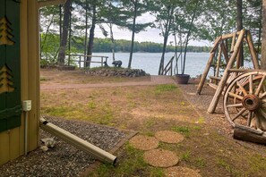 A wooden deck with a stone wall, a wooden bench, a wooden swing set, and a view of a lake surrounded by trees. - Charming lakefront home with dock, fireplace, streaming, lake views, W/D, & AC (Conover)