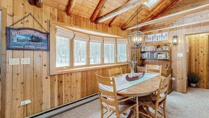 Ein Holzinterieur mit einem Esstisch, Stühlen, einer Deckenleuchte und einem Bücherregal.