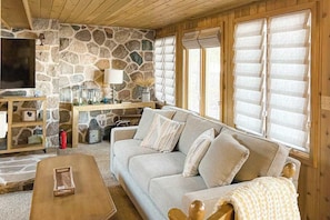 A cozy living room with a stone wall, a sofa, a coffee table, and a television. - Charming lakefront home with dock, fireplace, streaming, lake views, W/D, & AC (Conover)